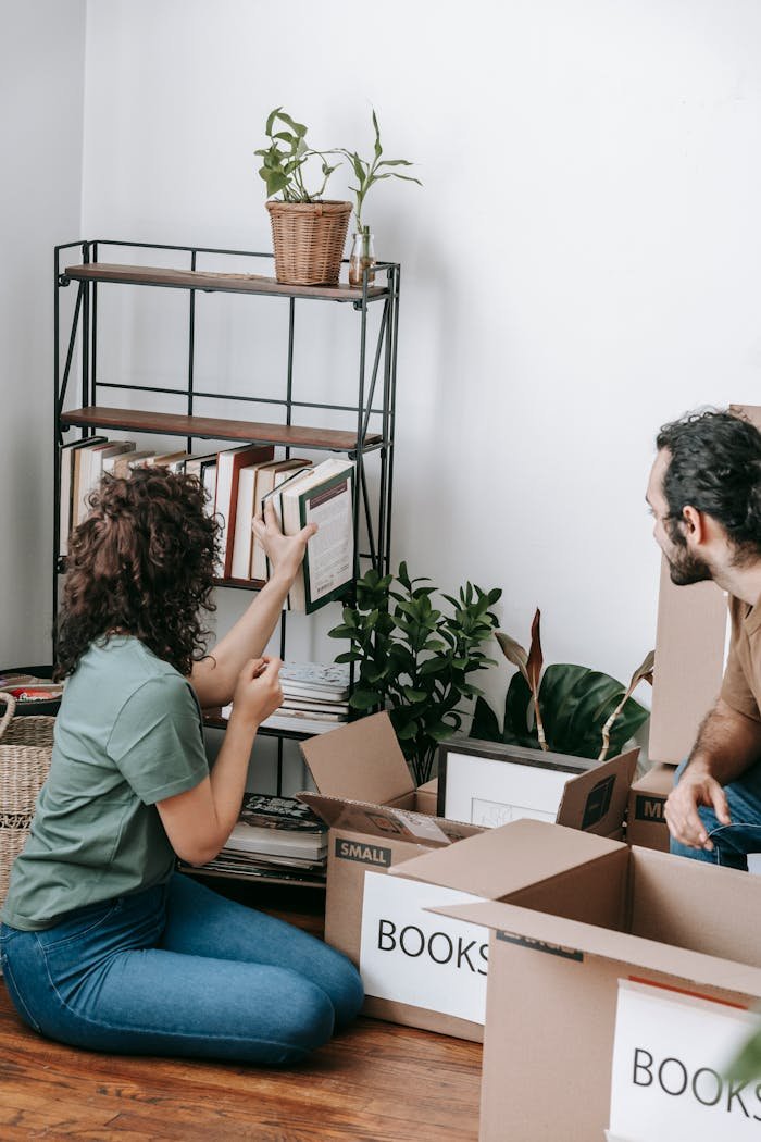 A couple packing books into boxes during a move in their contemporary apartment.
