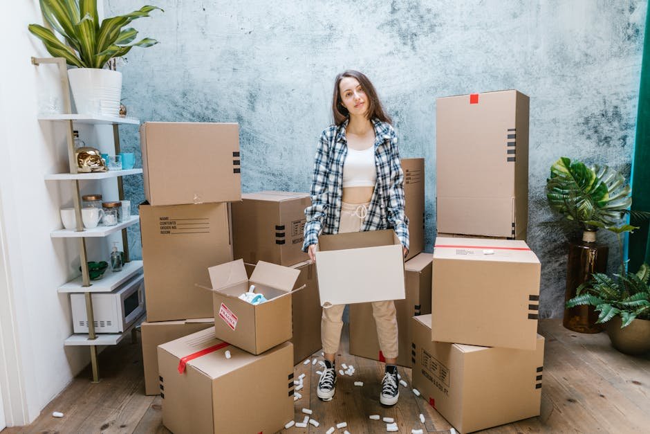 A woman organizing cardboard boxes filled with packing materials in a sunlit living room, preparing for a move.