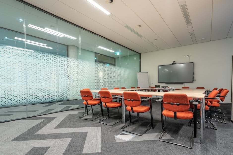 Spacious conference room with glass walls and orange chairs around a rectangular table.