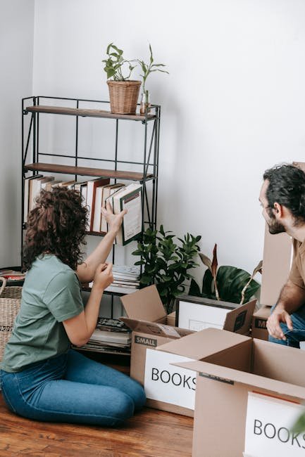 A couple packing books into boxes during a move in their contemporary apartment.